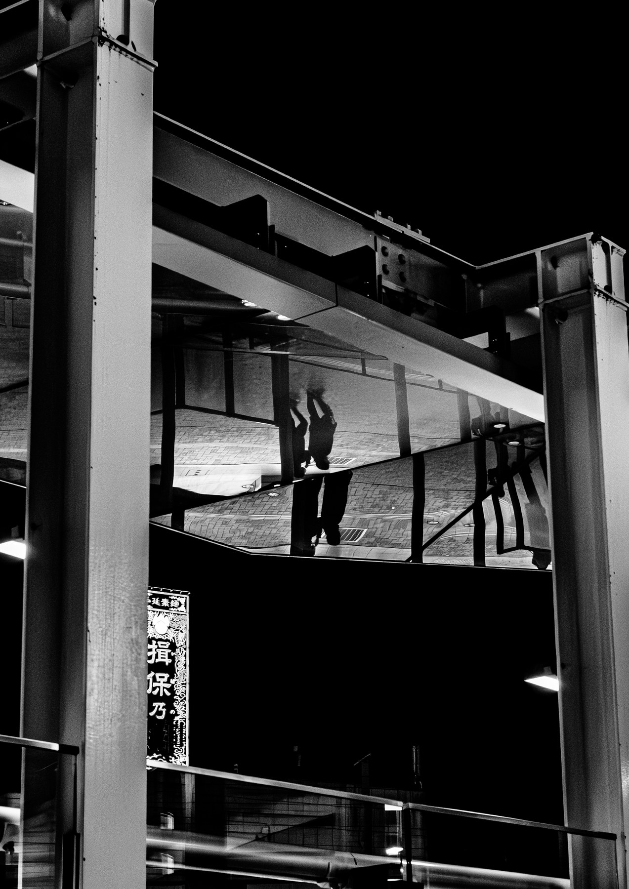 Black-and-white photograph of figures reflected upside down among steel beams and glass.